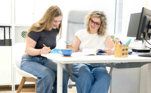 Eine junge Frau und eine Beraterin arbeiten gemeinsam an einem Schreibtisch.
